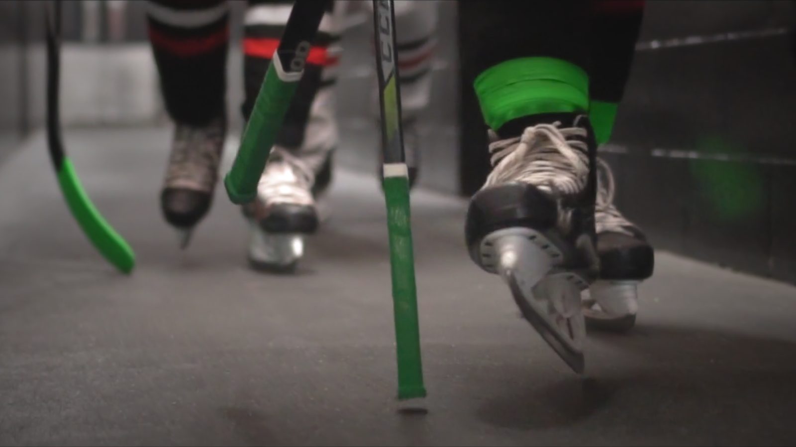 Skates and green-taped hockey sticks moving down an arena hallway